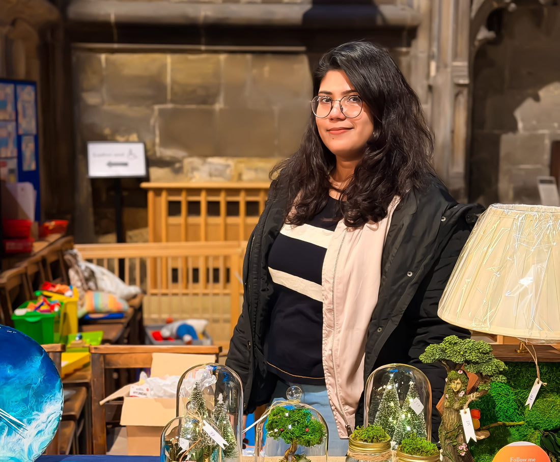 Nupur, a handmade moss and resin art creator, standing proudly behind her first-ever market stall filled with fairy garden terrariums, ocean resin clocks, and illuminated moss frames