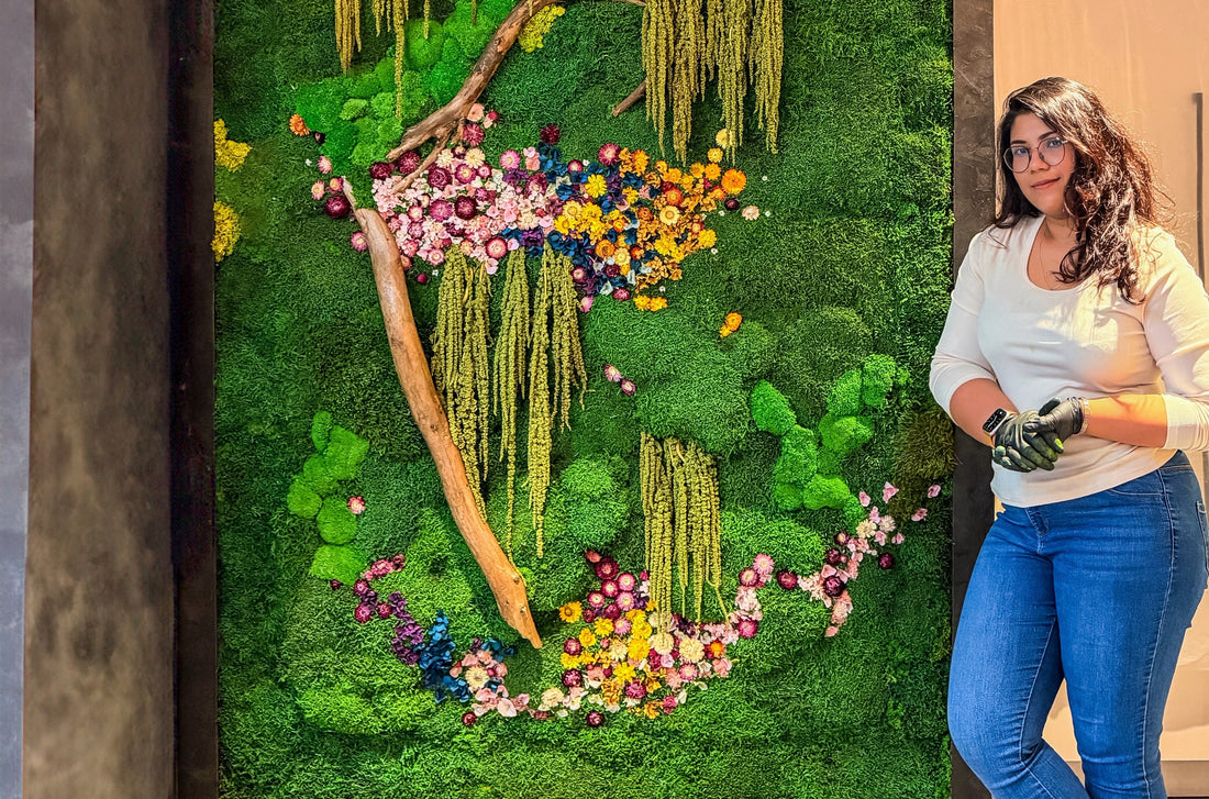 Artist Nupur Dasgupta standing next to a large vertical garden wall with preserved flowers