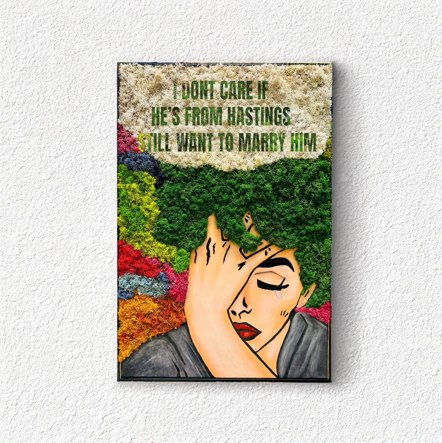 Framed artwork with a stylized face and text on a textured wall.