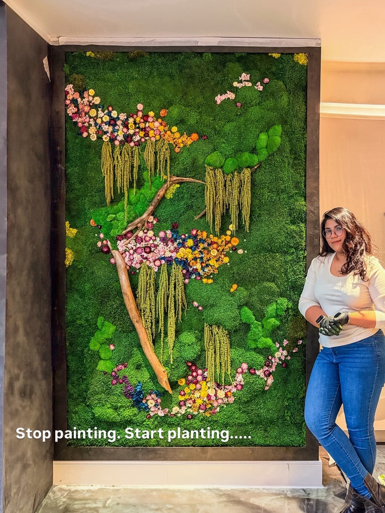Woman standing next to a large vertical garden wall with text 'Stop painting, Start planting'.
