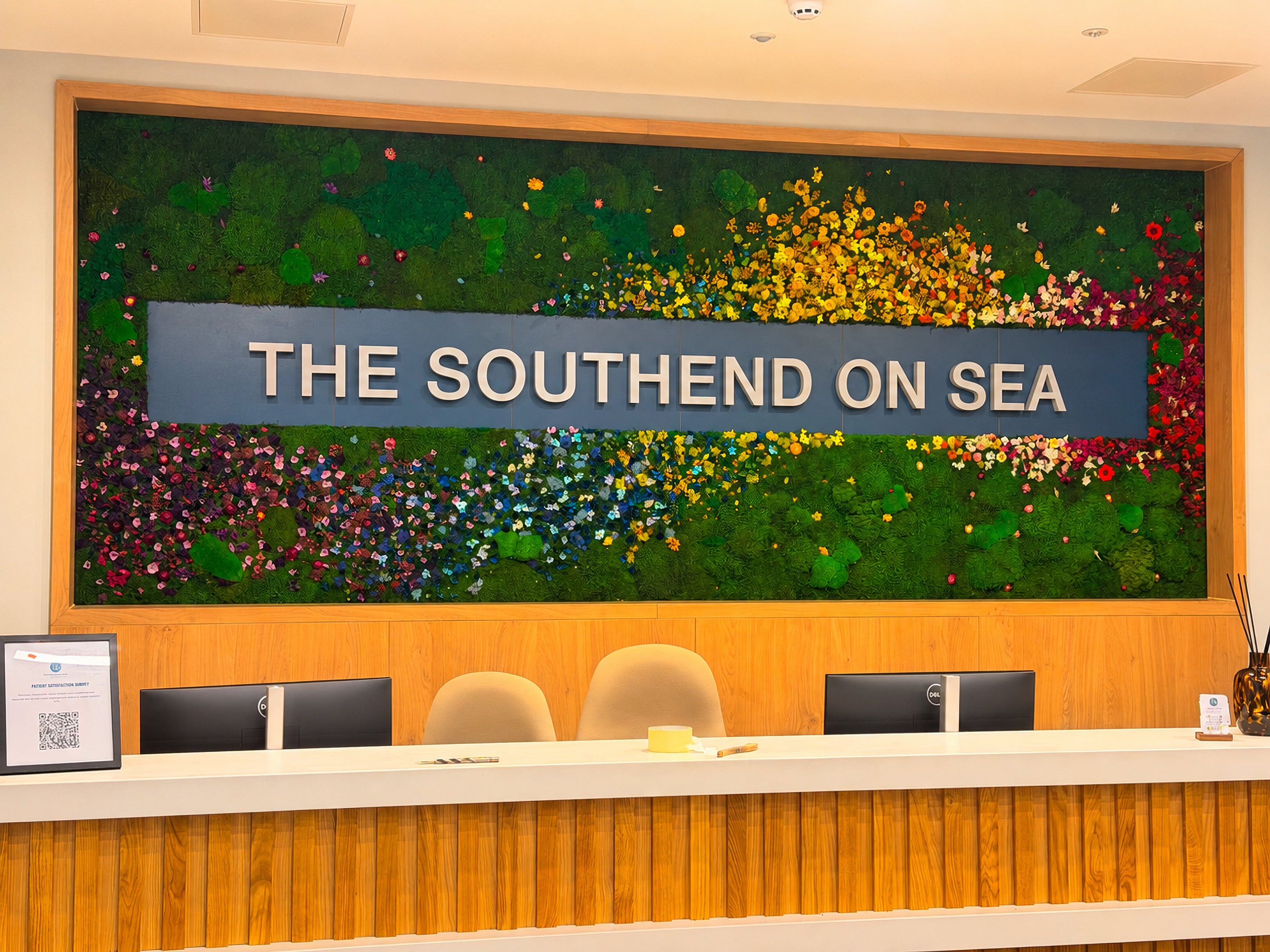 A large colorful wall mural with the text 'THE SOUTHEND ON SEA' across the center, mounted above a wood-paneled reception desk with chairs and computer monitors in a hotel or resort lobby.